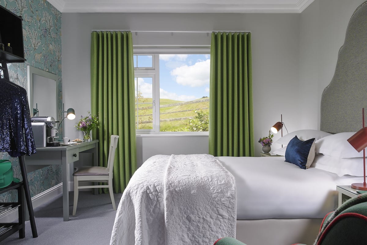 A bedroom with a bed, a desk, a chair, and a window with curtains.