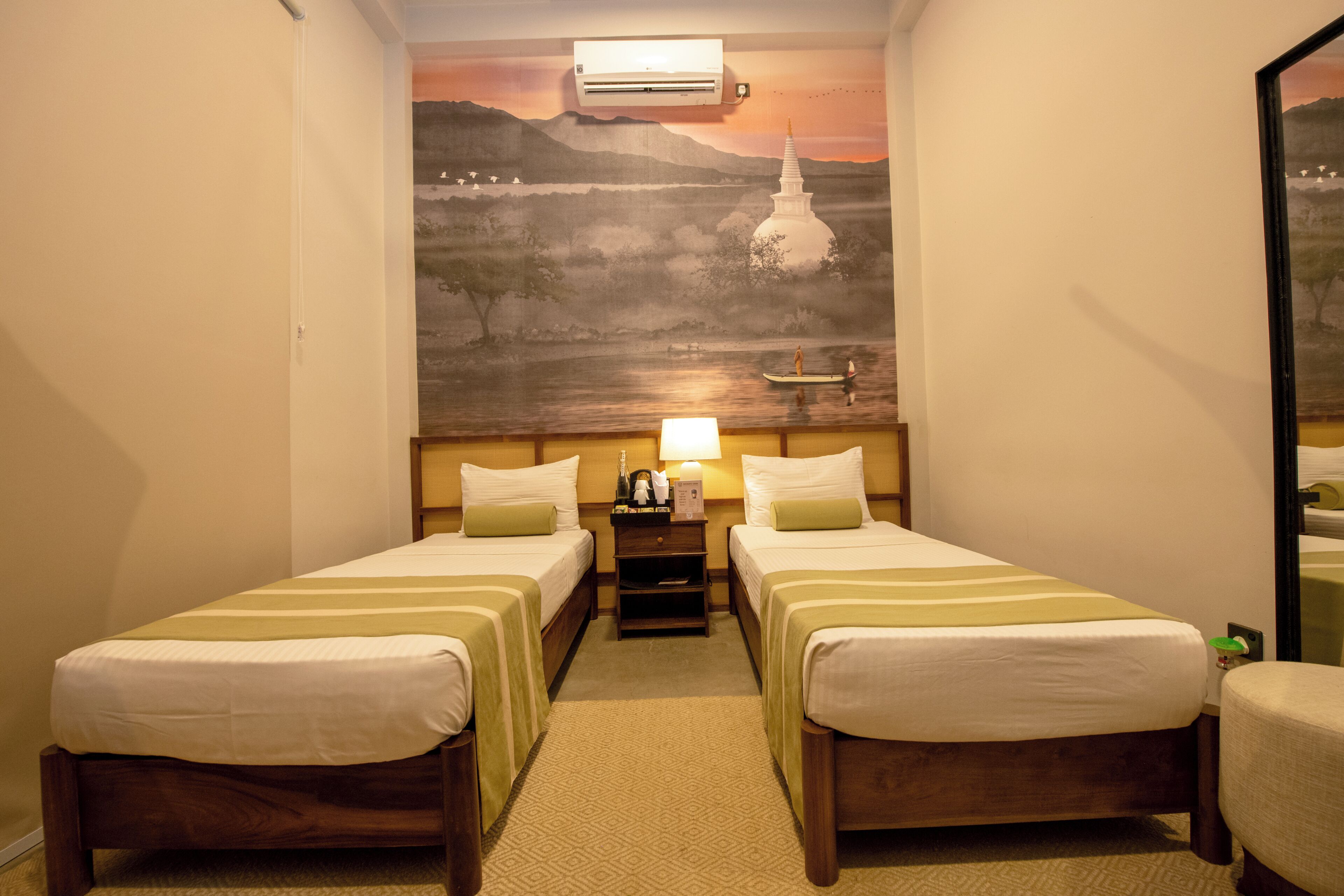 A hotel room with two beds, a nightstand, a lamp, and a wall mural.