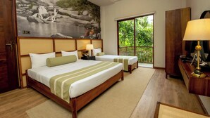 Ein Hotelzimmer mit zwei Betten, einem großen Wandgemälde eines Wasserfalls, einem Schreibtisch mit Lampe und Blick auf Grün durch ein Fenster.