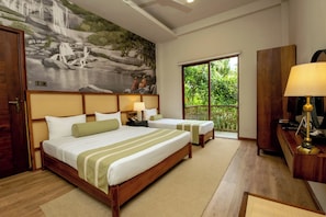 A hotel room with two beds, a large mural of a waterfall, a desk with a lamp, and a view of greenery through a window. - Kevans Casa (Mahiyanganaya)