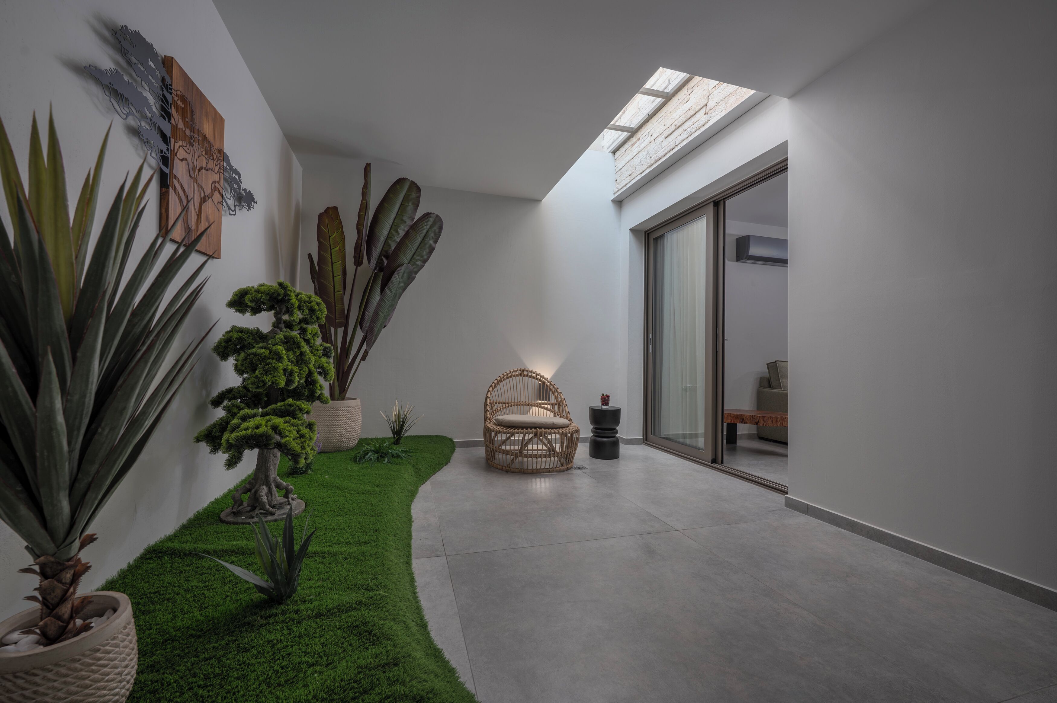 Un interior moderno con un vidrio que da a un balcón, una silla de mimbre y varias plantas en macetas.