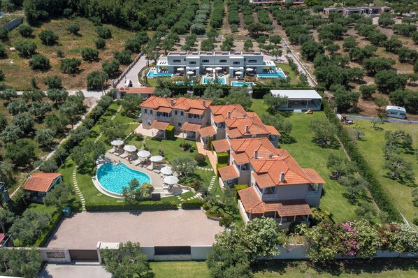 Vista aérea de un complejo turístico con varias villas, una piscina y un edificio grande con terraza.