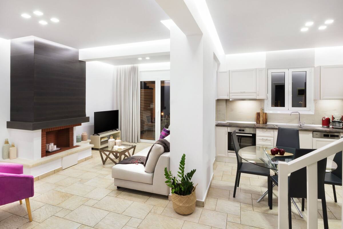 A modern living room with a fireplace, a sofa, a coffee table, and a dining area with a glass table and chairs.