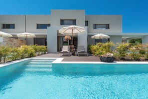 Un edificio moderno con piscina, asientos exteriores y sombrillas.
