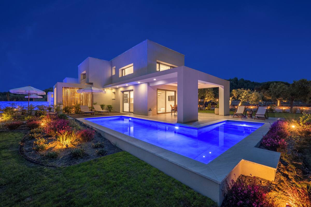 A modern two-story house with a swimming pool, outdoor seating, and well-lit landscaping.