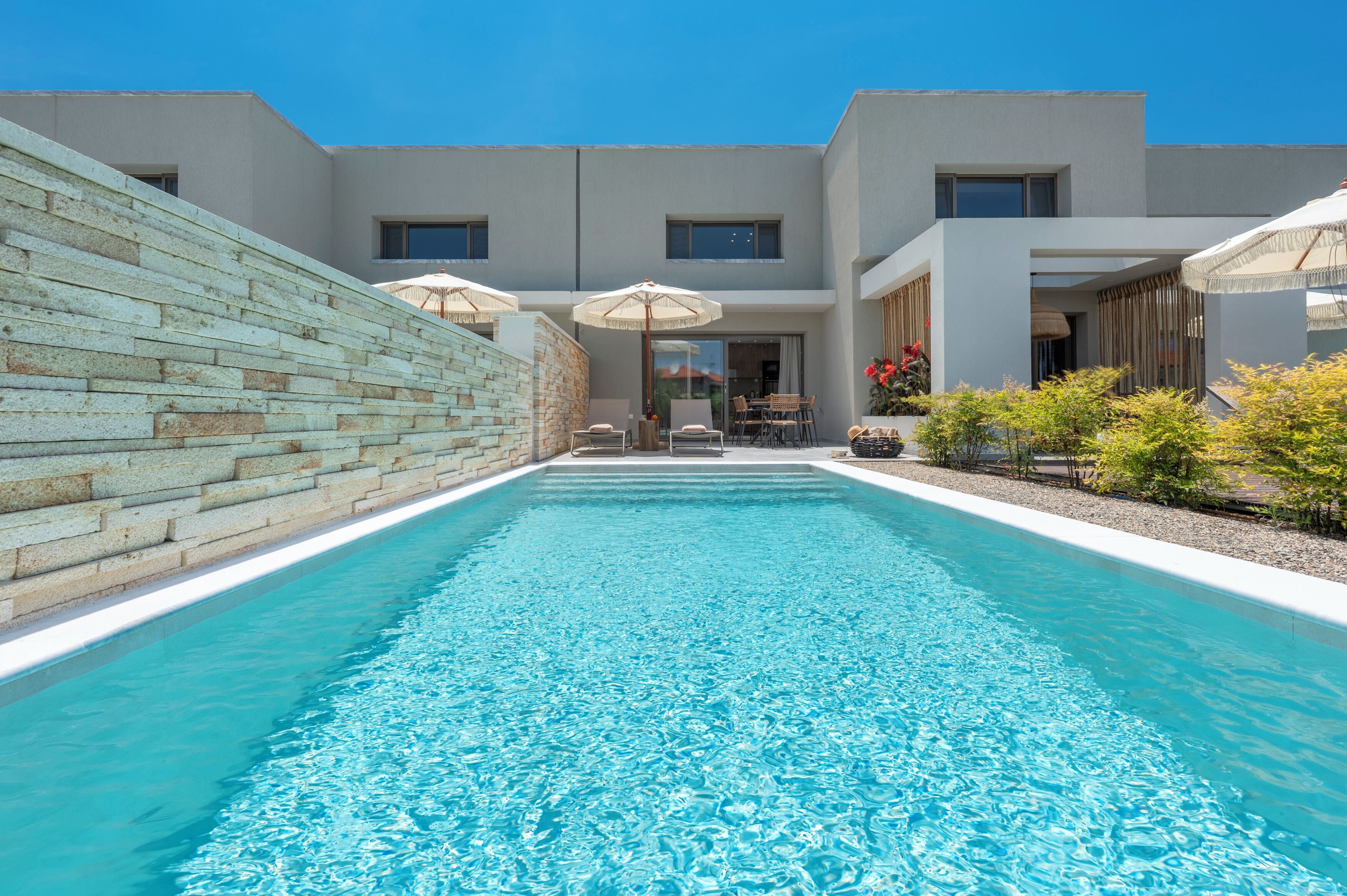 A modern building with a swimming pool, outdoor seating, and a stone wall.