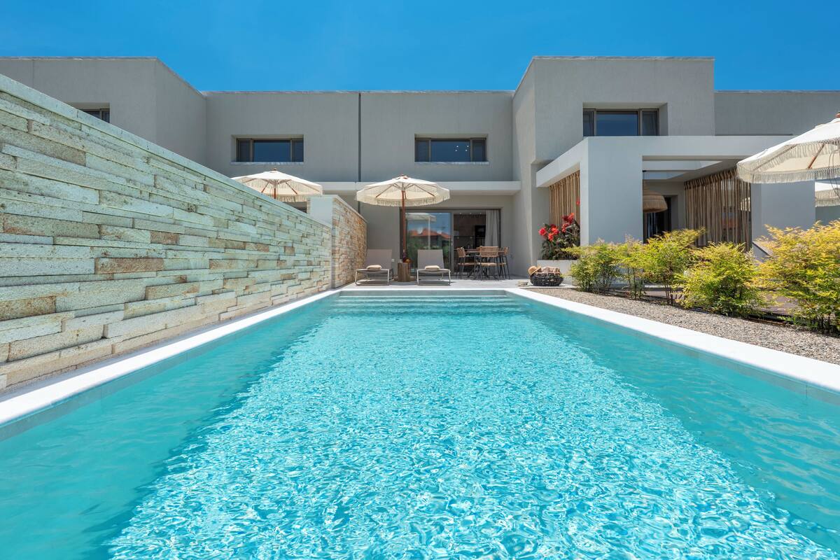 A modern building with a swimming pool, outdoor seating, and a stone wall.