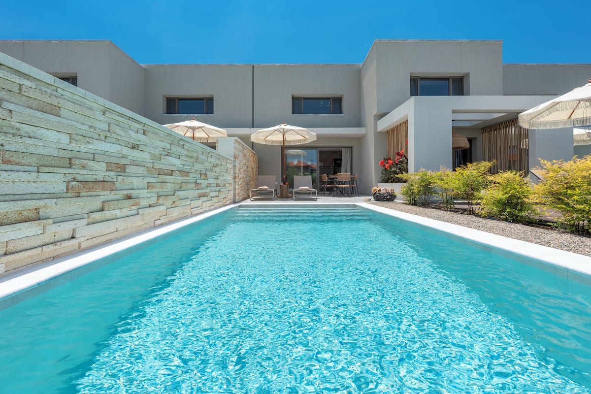 A modern building with a swimming pool, outdoor seating, and a stone wall.