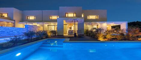 A modern house with a swimming pool, outdoor seating, and a well-lit entrance.