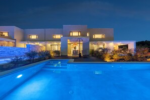 Una casa moderna con piscina, mobiliario de exterior e iluminación en la entrada.