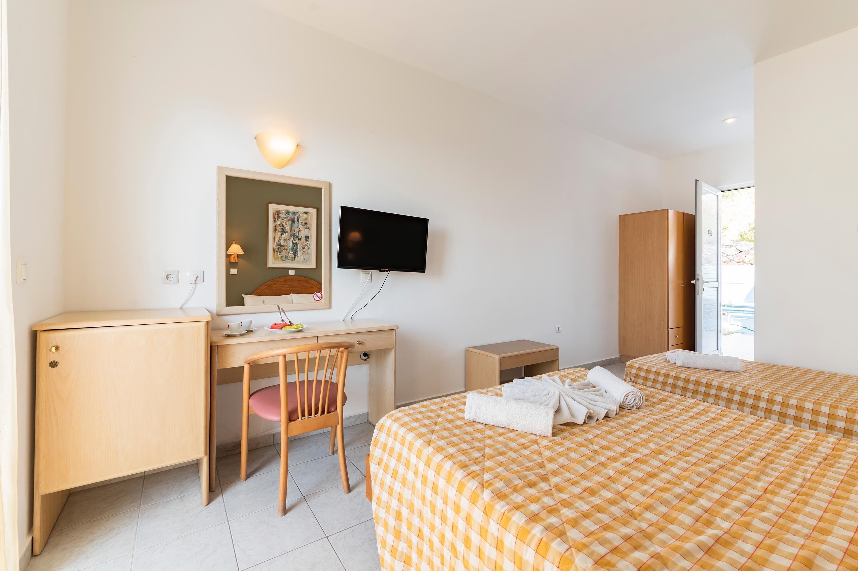 A hotel room with a desk, chair, bed with checkered bedding, a television, and a wardrobe.