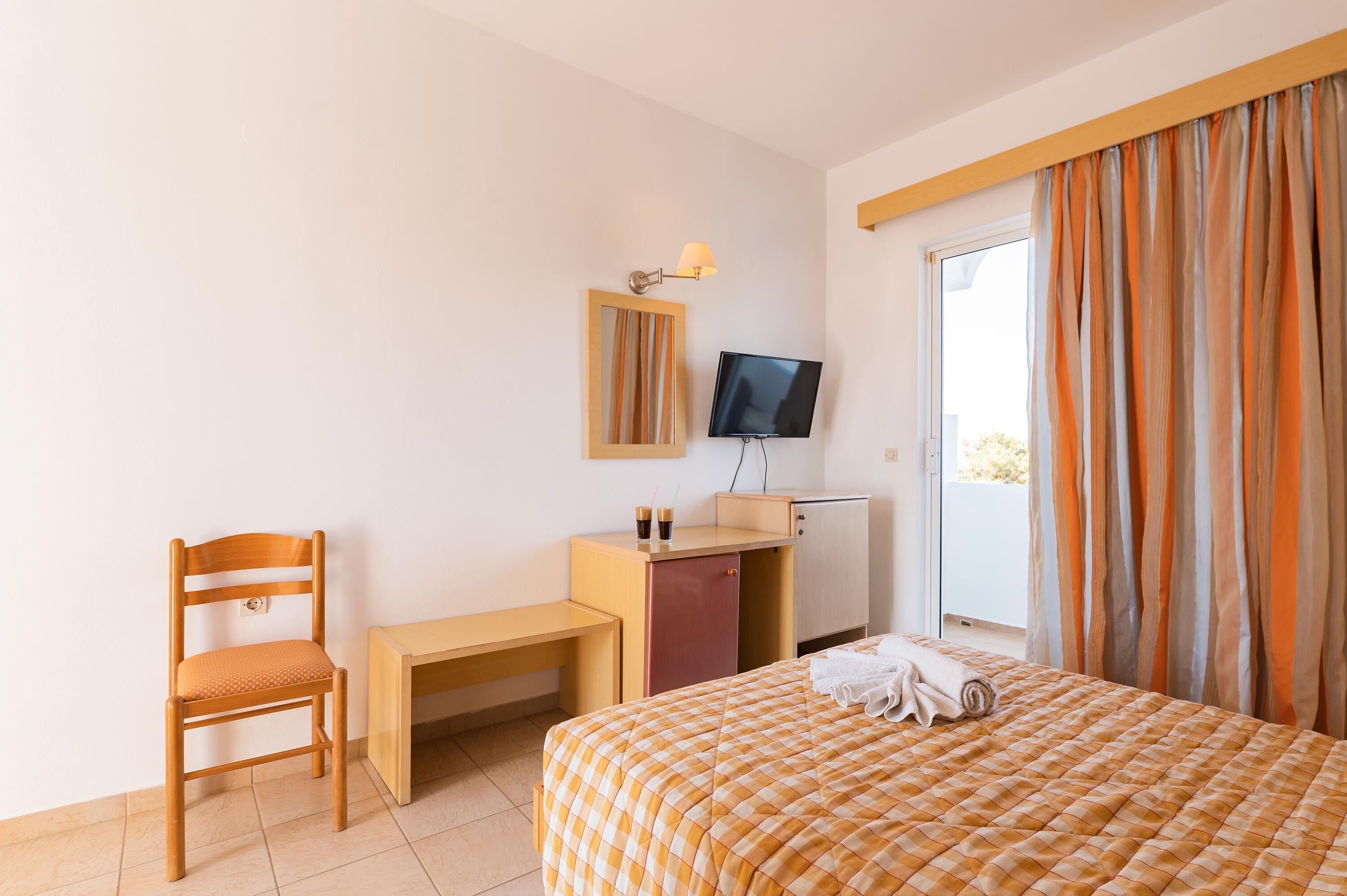 A hotel room with a bed, a desk, a chair, a TV, and a wardrobe.