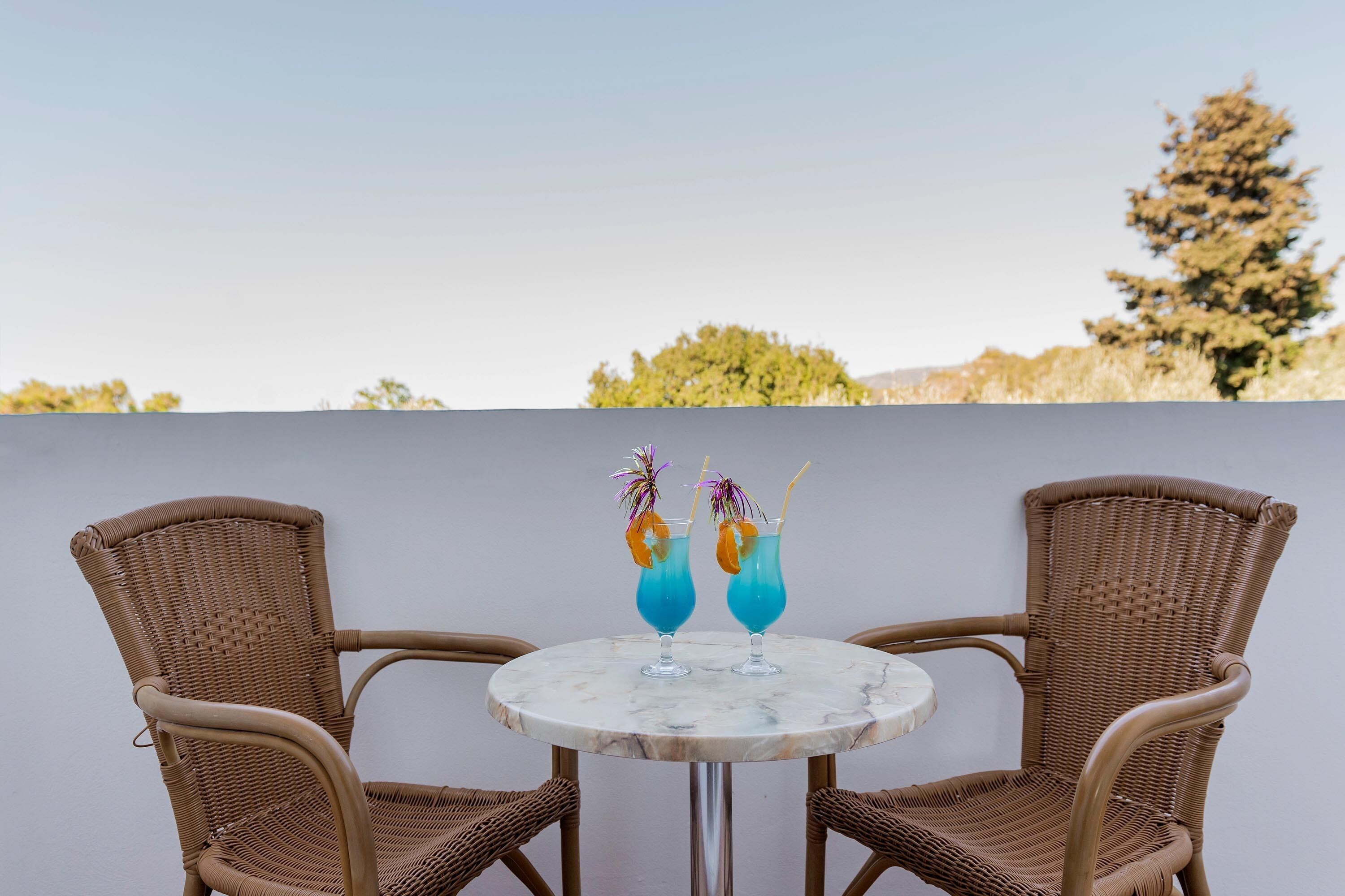 Une table ronde, deux chaises en osier et deux boissons contenant un liquide bleu et des décorations.