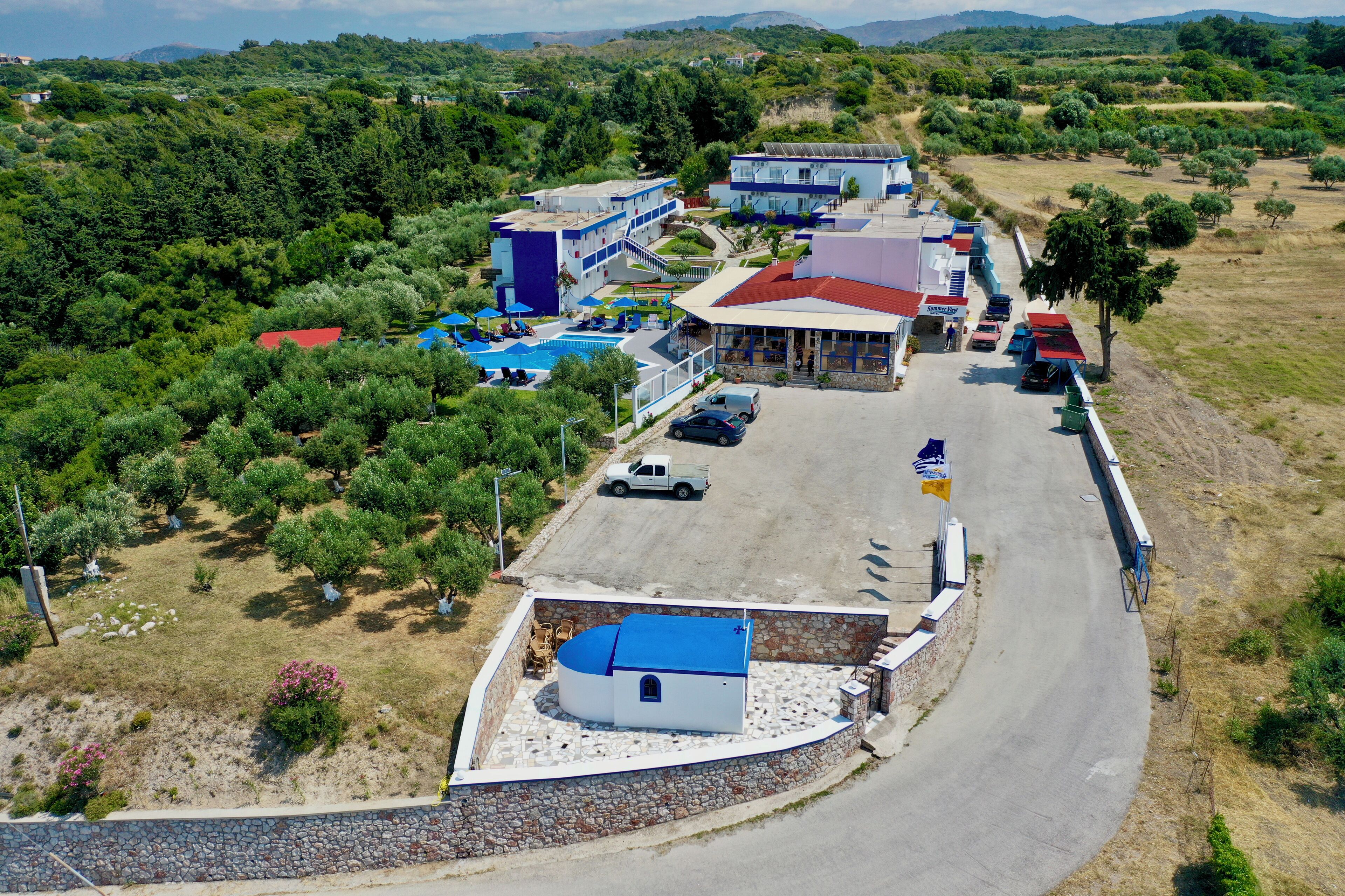 A hotel with a swimming pool, a parking area, and a view of the surrounding landscape.