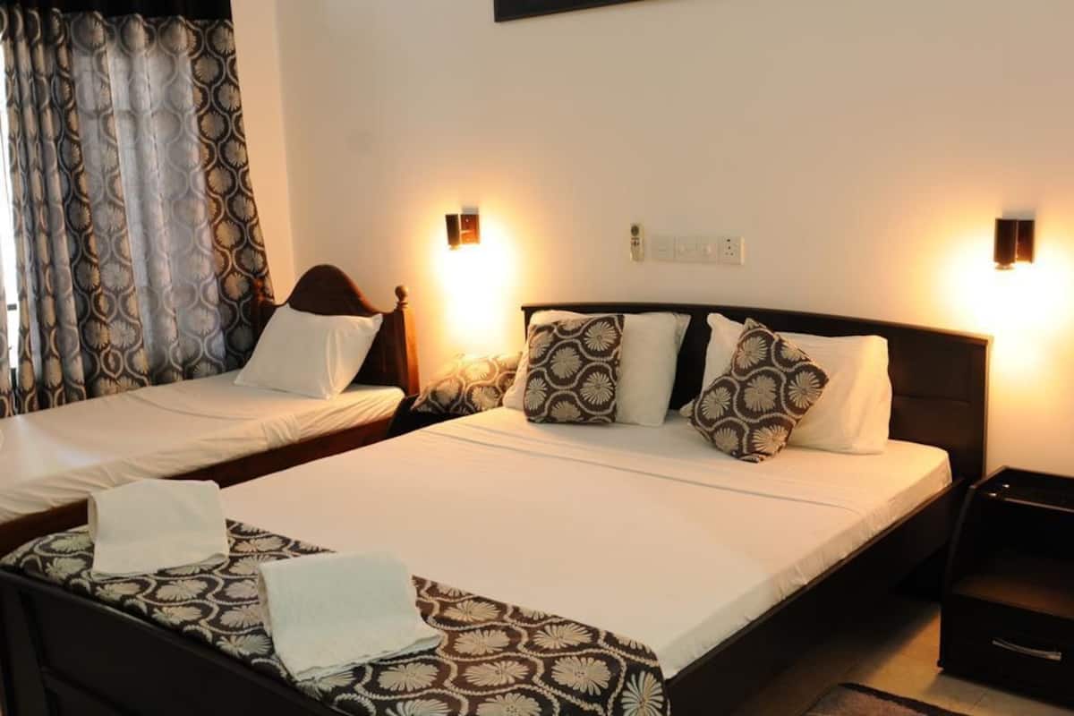 Une chambre d’hôtel avec deux lits simples, chacun agrémenté de draps et d’oreillers à motifs. Des lampes murales sont fixées au-dessus de chaque lit, et une petite table de chevet avec une lampe se trouve à côté des lits.