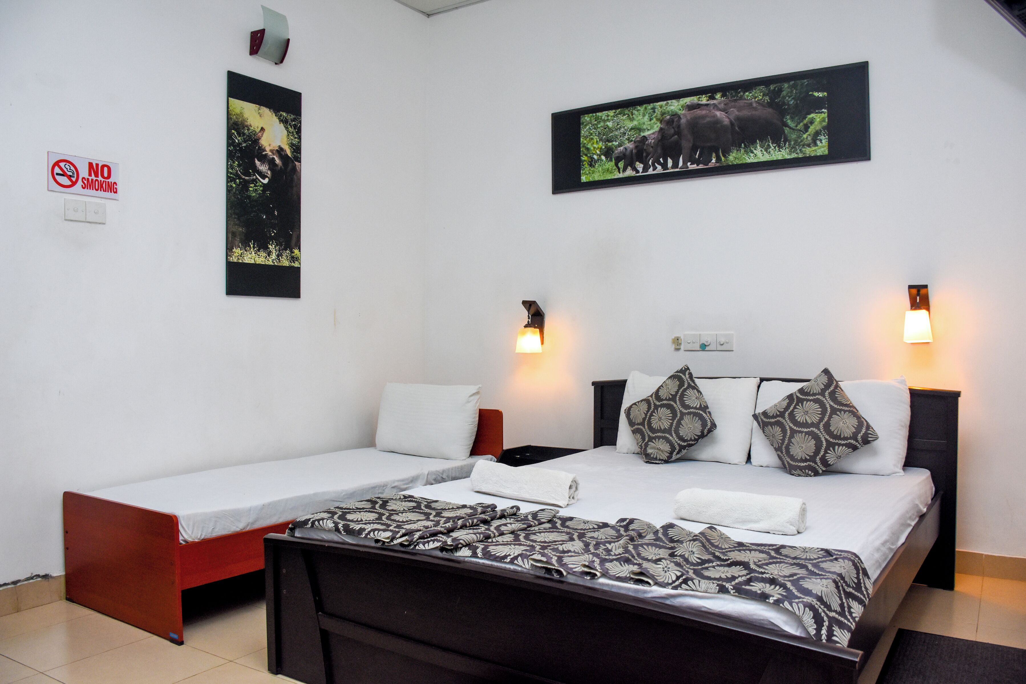Una habitación de hotel con una cama, un sofá cama, un cartel de 'NO FUMAR' y dos cuadros en la pared.