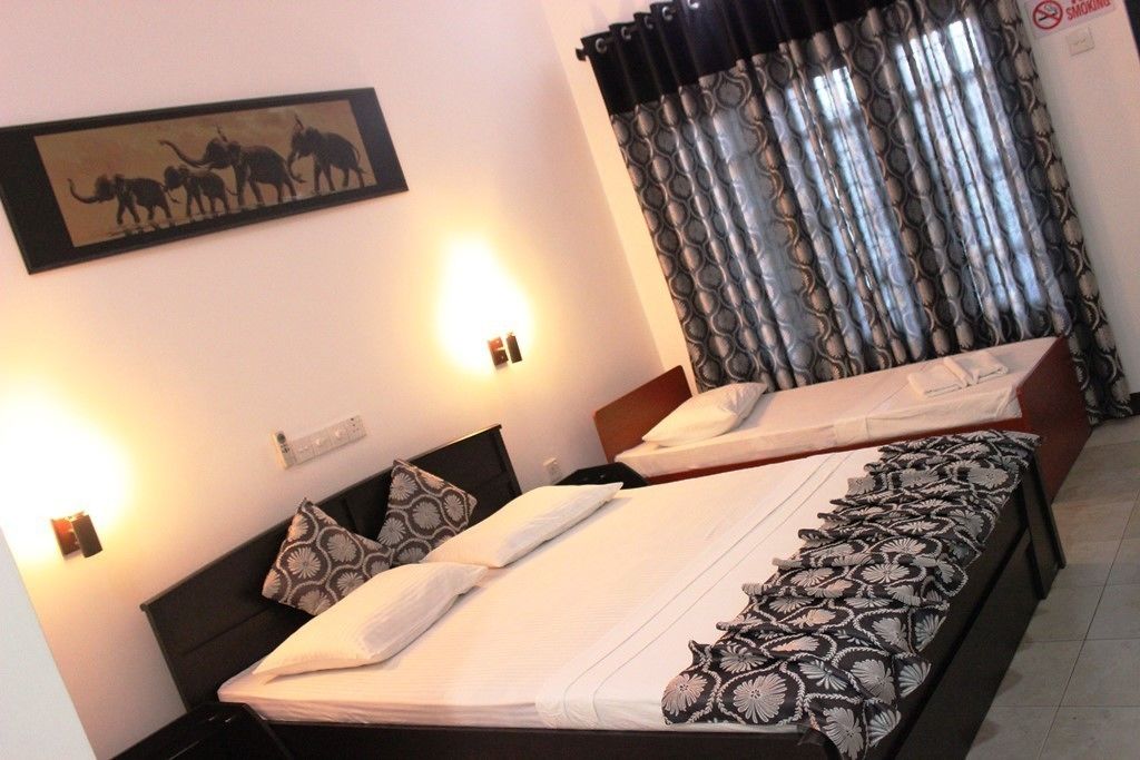 A hotel room with two beds, a wall-mounted artwork of elephants, a curtain, and a 'No Smoking' sign.