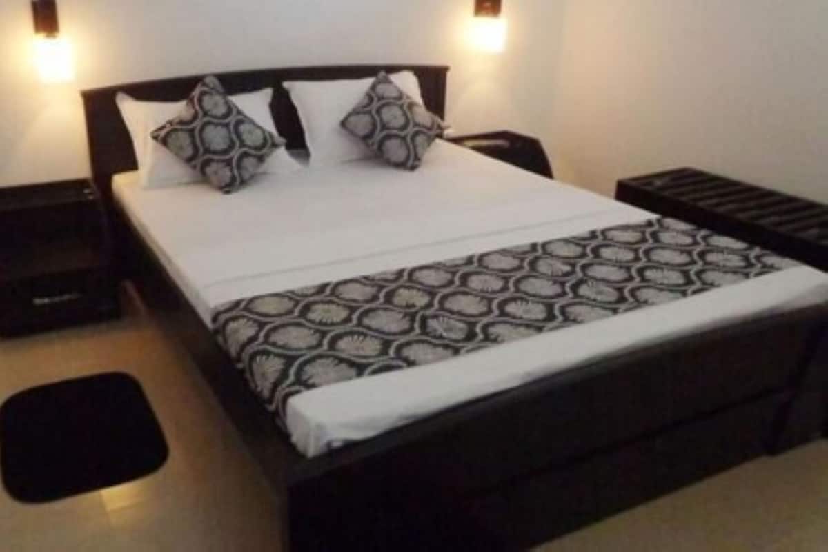 Un lit avec une couvre-lit à motifs, deux oreillers, une table de chevet noire et un petit tapis noir.