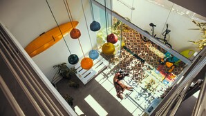 Un atrium à plafond haut, agrémenté d’une planche de surf, de lampes sphériques suspendues et d’un vélo.