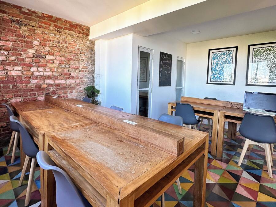 A conference room with a long wooden table, chairs, a brick wall, and colorful geometric-patterned flooring.