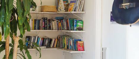 A room with a bookshelf, a guitar, and potted plants.