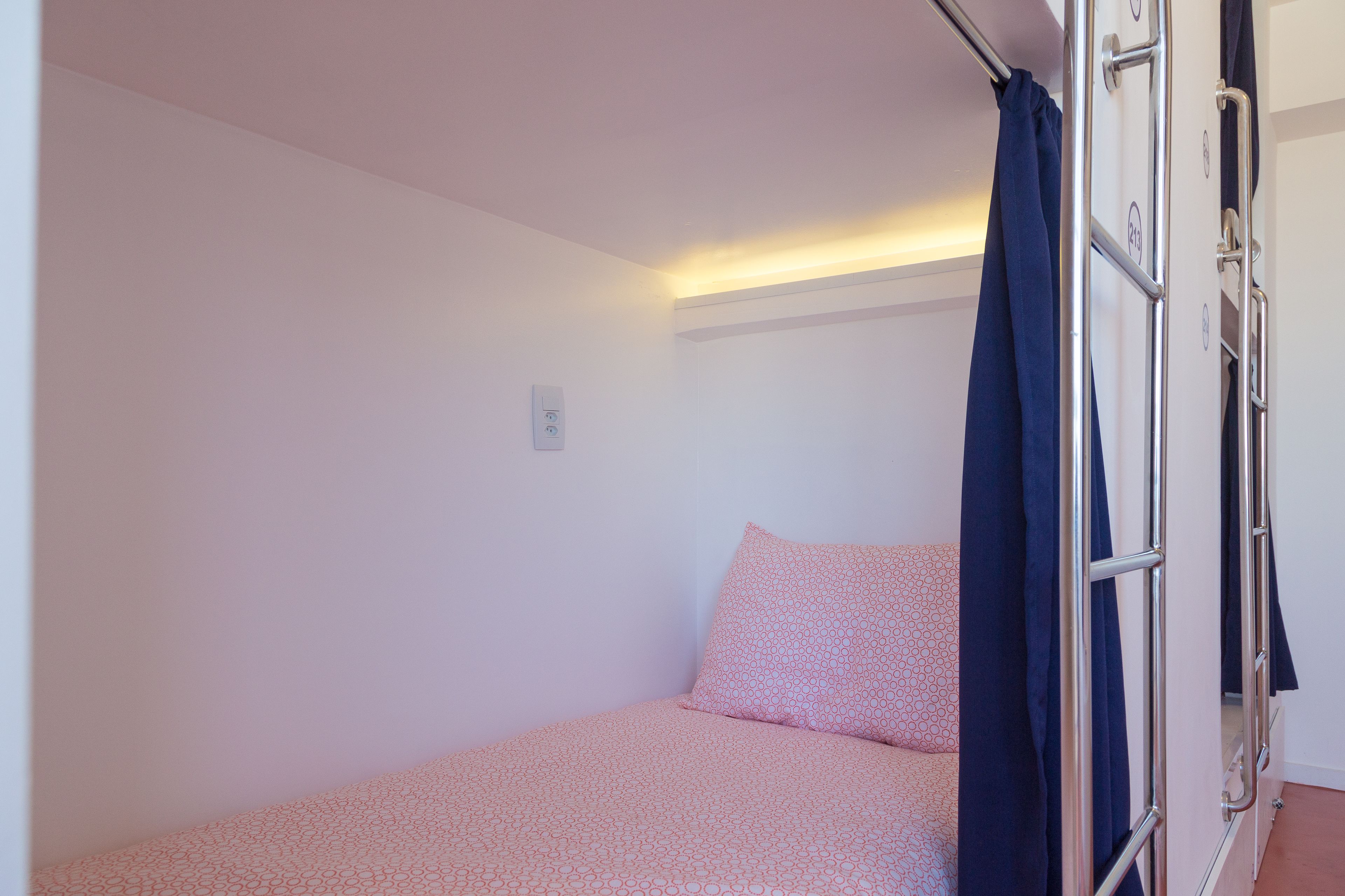 Une petite chambre avec un lit simple, une couvre-lit à motifs, une table de chevet et un rideau.