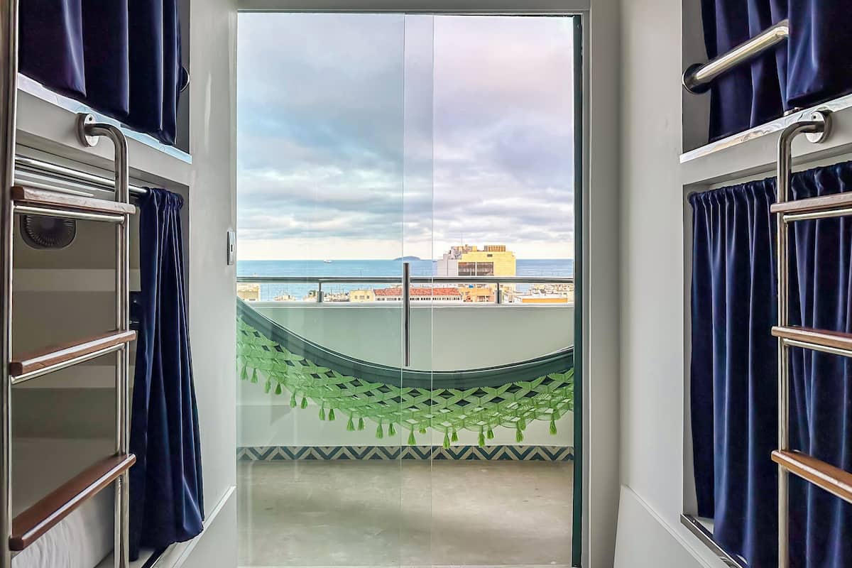 Een balkon met uitzicht op zee en gebouwen, een glazen deur en een groene decoratieve plant.