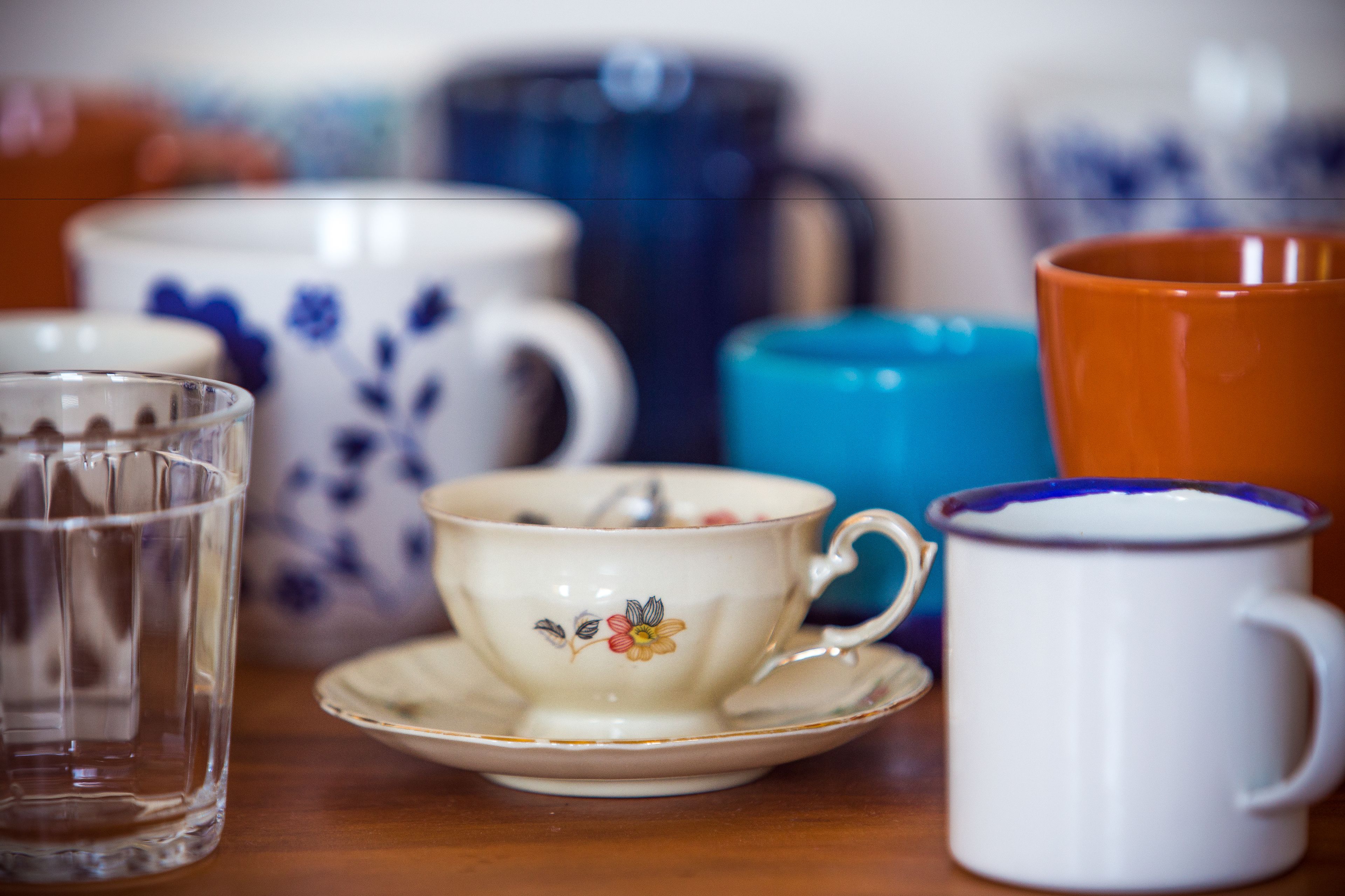 Une variété de tasses en céramique et un verre sont posés sur une table en bois.