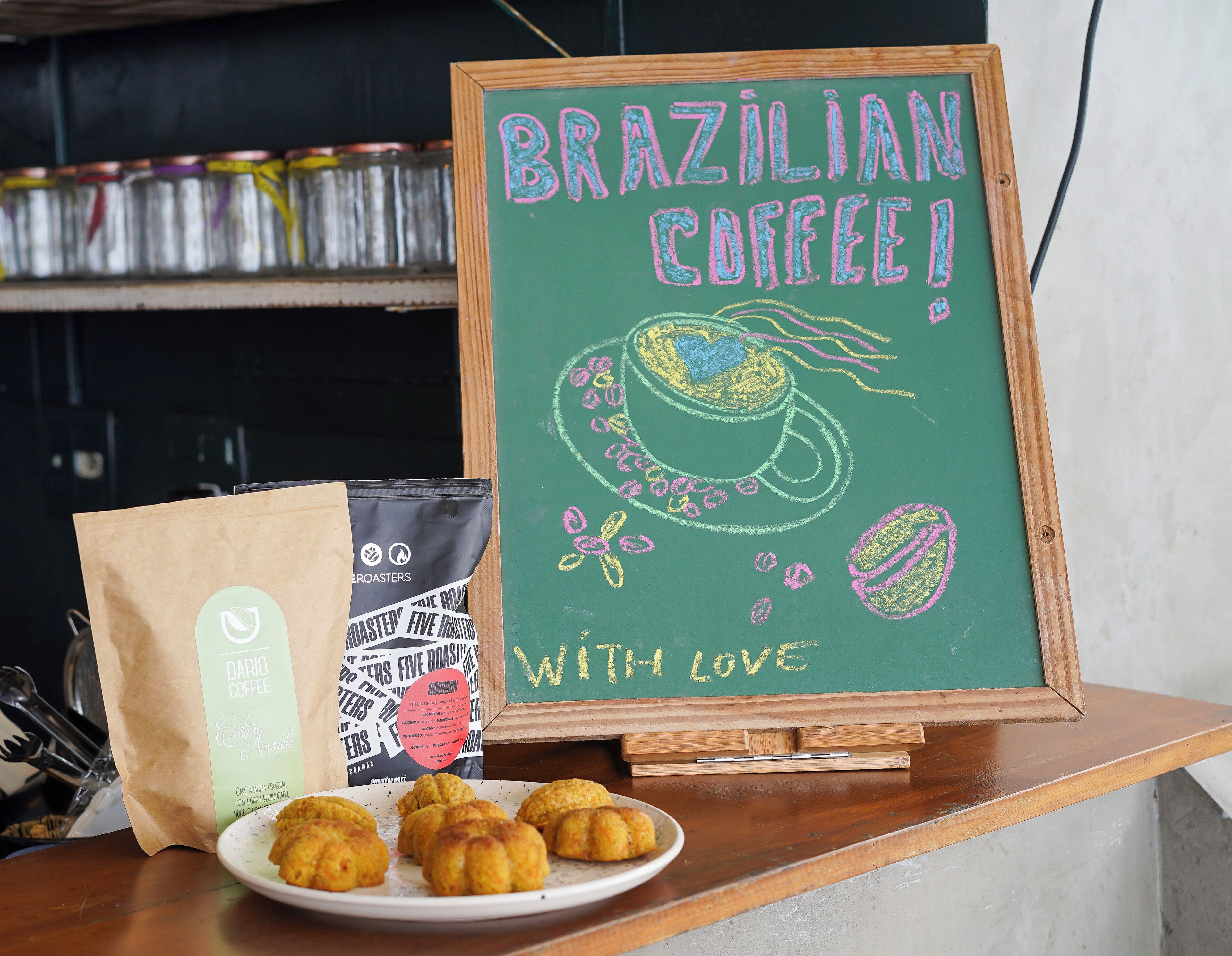 A chalkboard with 'Brazilian Coffee!' written on it, a coffee bag, and a plate of pastries.