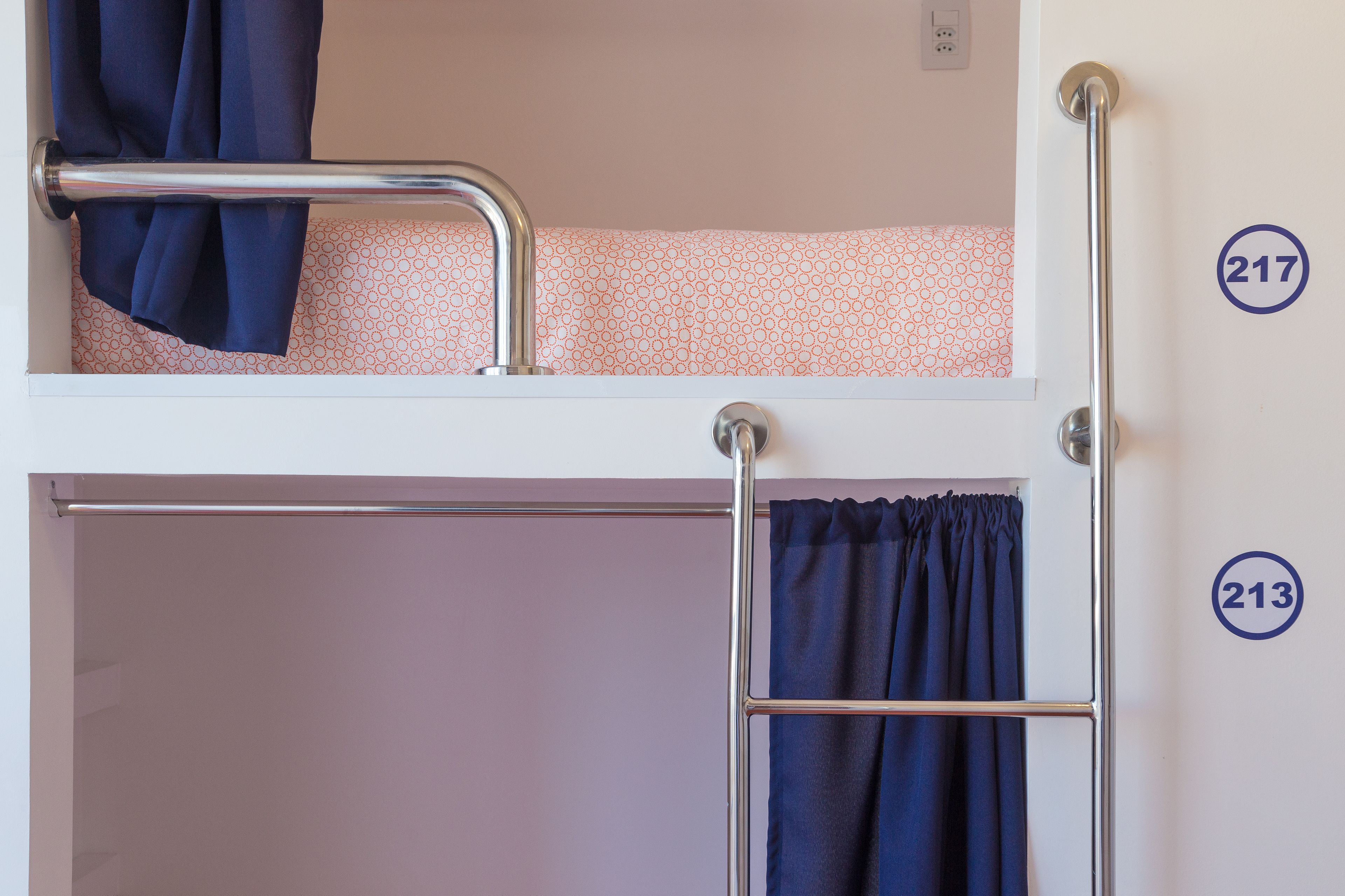 A bunk bed with a metal ladder and a curtain. Numbers 217 and 213 are visible on the wall.
