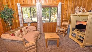 A cozy room with a sofa, a wooden coffee table, a TV stand with a flat-screen TV, and a window with curtains. - 1198 Carson Avenue 1 Bedroom Cabin by RedAwning (South Lake Tahoe)