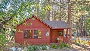 A small, red cabin with a porch, surrounded by trees and a gravel driveway. - 1198 Carson Avenue 1 Bedroom Cabin by RedAwning (South Lake Tahoe)