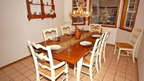 A dining area with a wooden table, white chairs, a chandelier, and a window with a view. - 1209 Golden Bear 3 Bedroom Home by RedAwning (South Lake Tahoe)