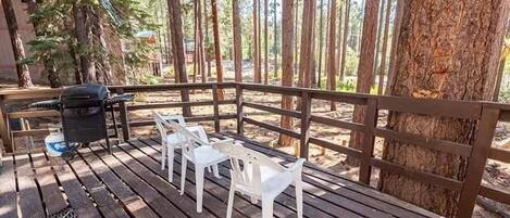 A wooden deck with white plastic chairs and a grill.