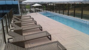 Un  área de piscina en la azotea con sillones de descanso y barandilla de cristal.
