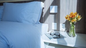 Una habitación de hotel con una cama bien hecha, una mesita de noche con un florero y una revista.