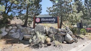 A sign for Heavenly California Lodge surrounded by a stone wall and pine trees. - 1510 Wildwood, 6 2 Bedroom Condo by RedAwning (South Lake Tahoe)