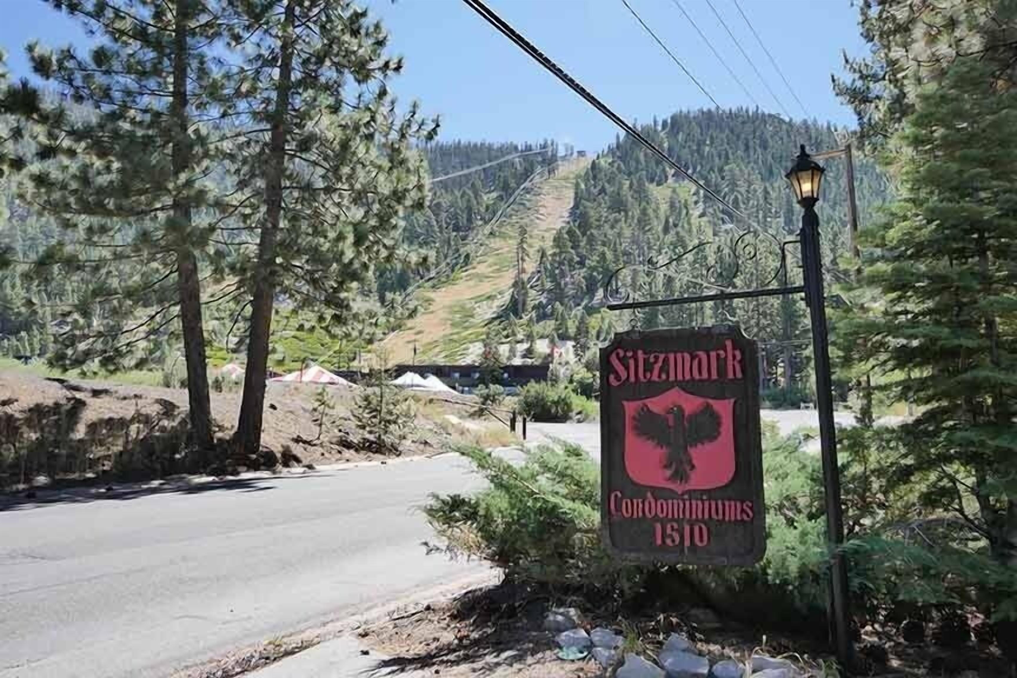 A sign with the text "Sitzmark Condominium 1510" in a natural setting with trees and a road.
