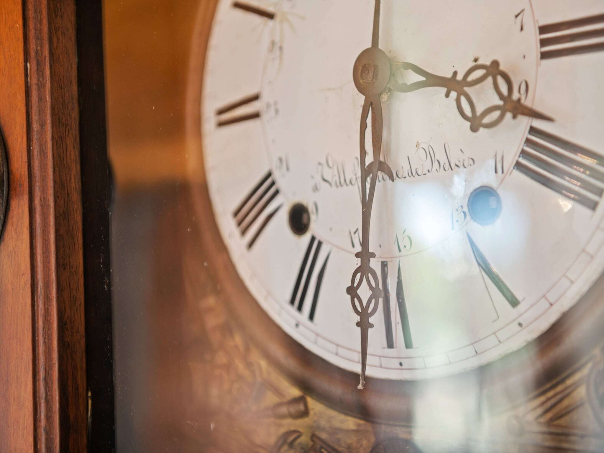 A close-up of a clock face with Roman numerals and a pendulum.