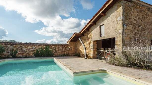 Un bâtiment en pierre avec une piscine, une clôture en bois et un ciel dégagé.