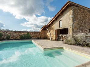 Un edificio de piedra con piscina, cerca de madera y cielo despejado.