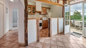 Une cuisine avec des poutres en bois, un réfrigérateur blanc et, derrière une porte vitrée, une vue sur un espace extérieur.