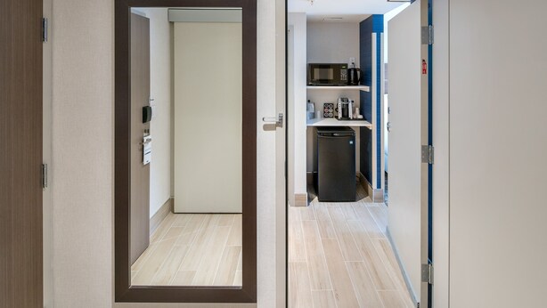 A hallway with a door leading to a room with a microwave and coffee maker on a shelf. - Holiday Inn Express Red Deer North by IHG (Red Deer)