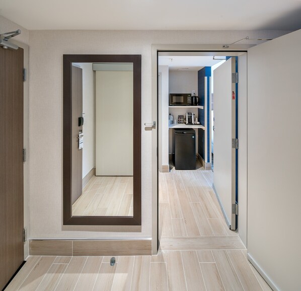 Un pasillo con una puerta que da a una habitación con microondas y cafetera sobre una estantería.