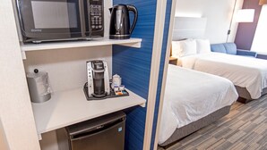 A hotel room with a microwave, coffee maker, and a small refrigerator. There is a bed with white bedding and a blue accent wall. - Holiday Inn Express Red Deer North by IHG (Red Deer)