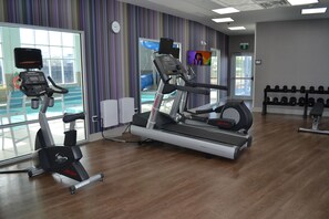 Un gimnasio con cintas de correr, elípticas y un estante de mancuernas.