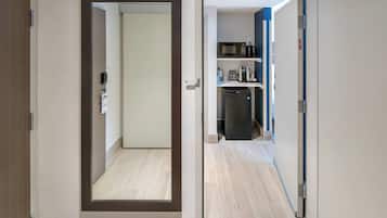 Un pasillo con una puerta que da a una cocina con microondas, cafetera y refrigerador.