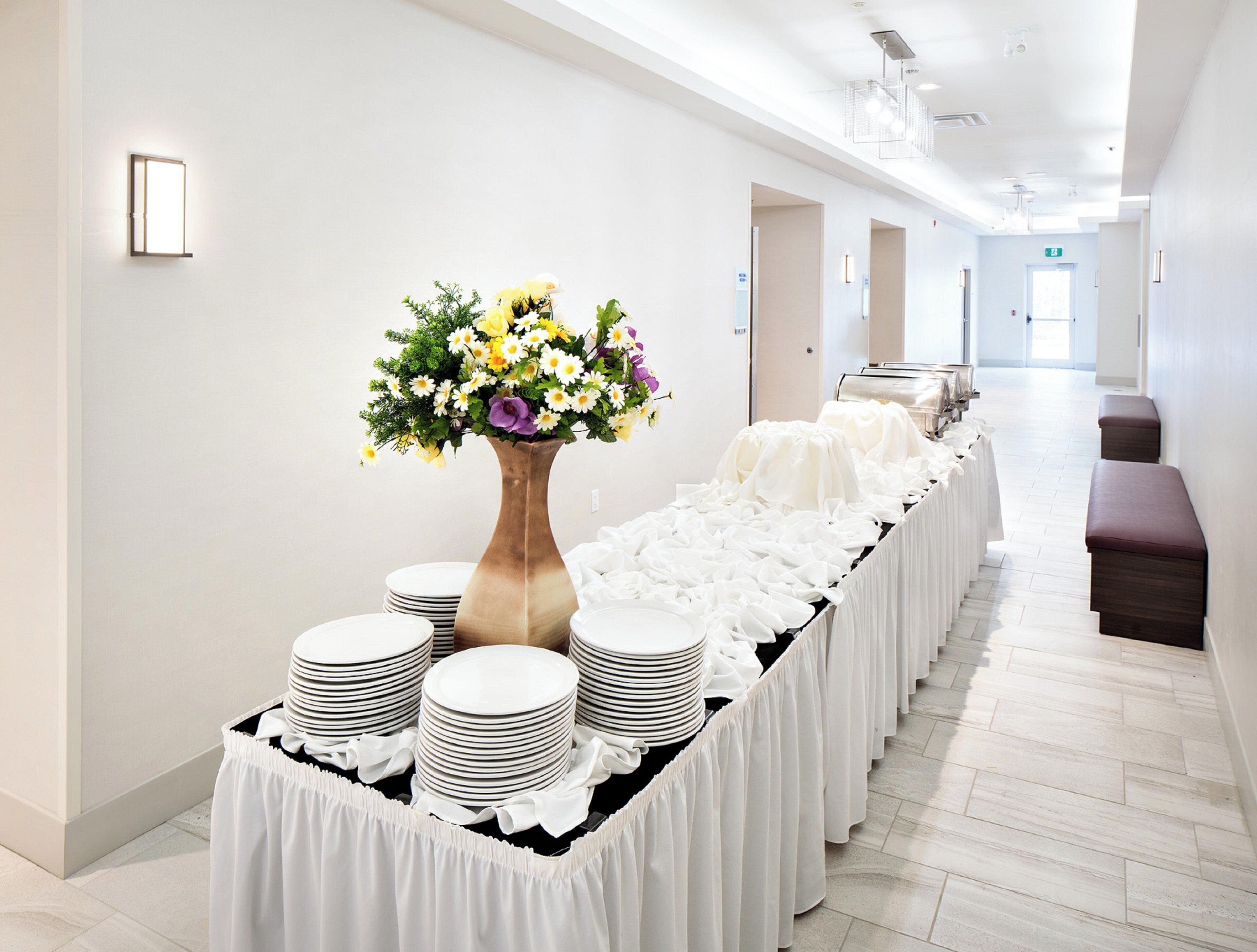 A hotel corridor with a long table set with white tablecloths, plates, and a vase of flowers.