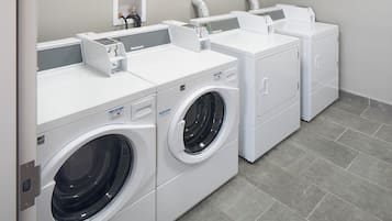 A row of white front-loading washers and dryers in a commercial setting.