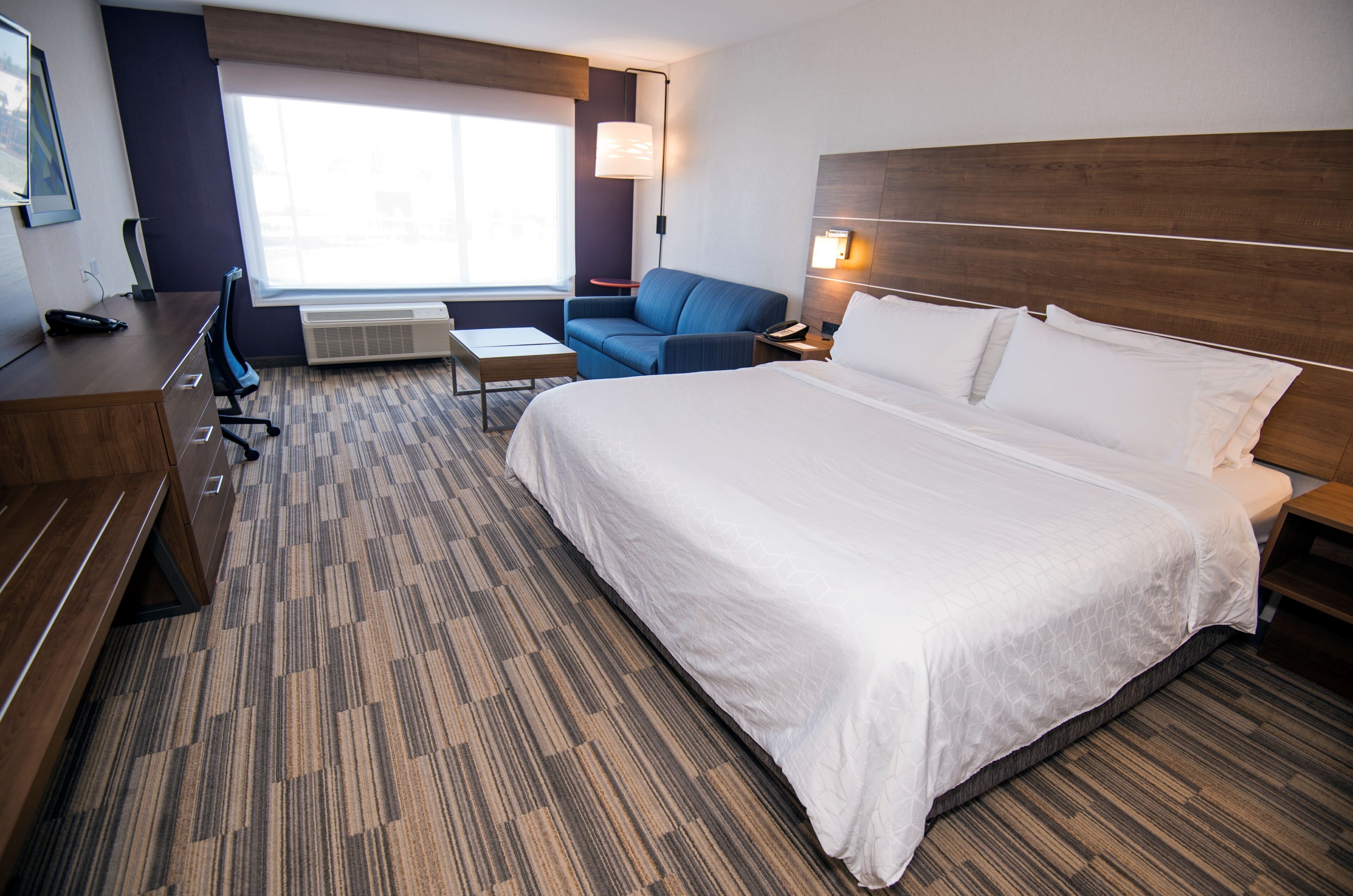 A hotel room with a large bed, a desk, a chair, a small table, and a sofa.